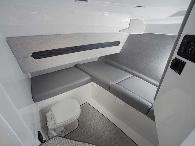 Cobalt A29 day cabin with head compartment featuring a marine toilet, upholstered bench seating, and soft-lit white interior