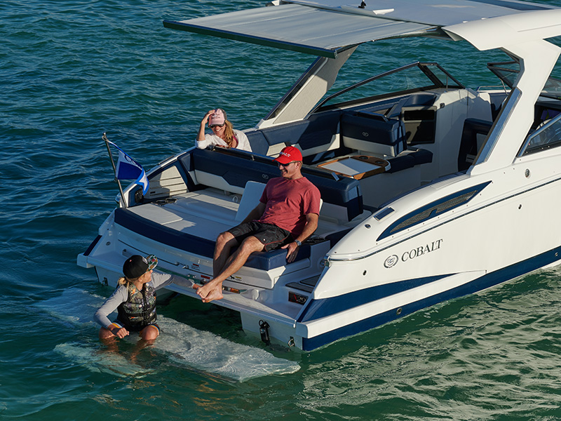 Cobalt A29 with Makefast powered sun awning extended from hardtop over the aft deck with passengers relaxing in shade on open water