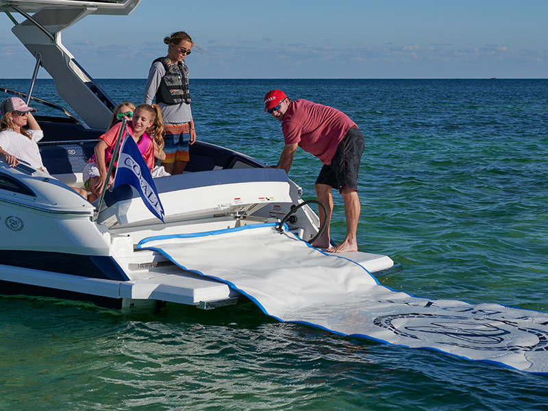 Family on the Cobalt A29 stern swim platform deploying the Splash and Stow branded inflatable float mat on clear turquoise water