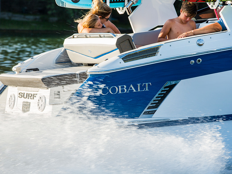 Two Cobalt surf boats with COBALT hull graphics running side by side at speed with water spray