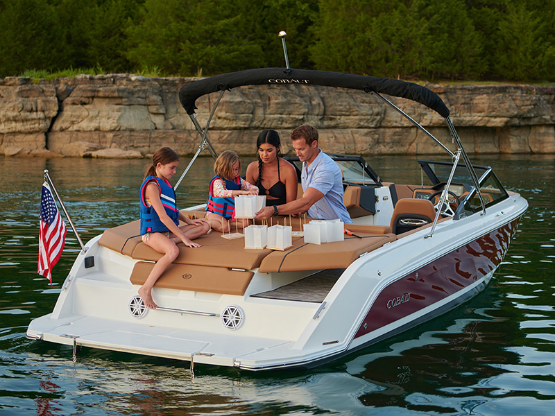 Family on a red Cobalt CS22 at speed on a lake with black bimini top deployed showing full-width bow sunpad seating area