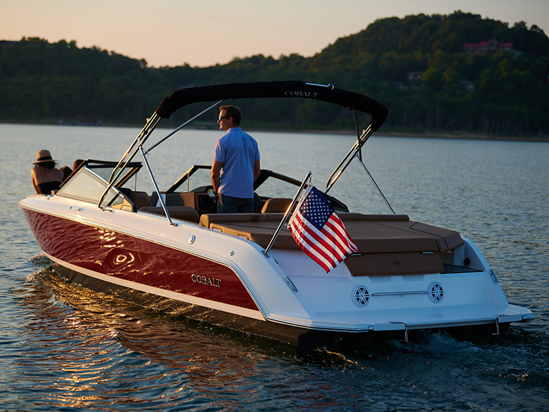 Man at the helm of a red Cobalt CS22 at sunset on a calm lake with American flag showing the distinctive wave style-line hull graphics