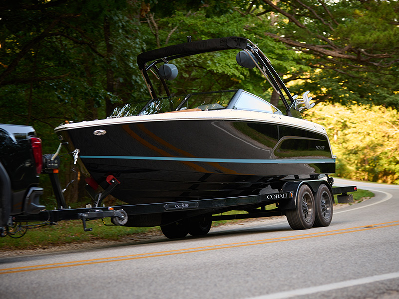 Black and tan Cobalt CS23 Surf on trailer being towed down a wooded two-lane highway demonstrating easy trailerable size