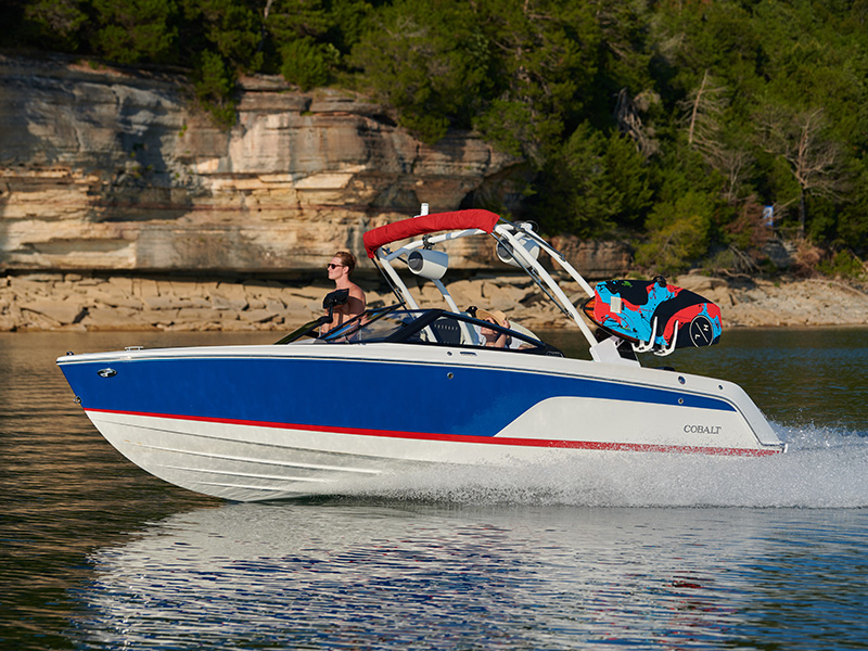 Cobalt CS23 Surf running at speed on a lake with bold blue, red, and white surf hull graphics and surf tower with wakeboard rack