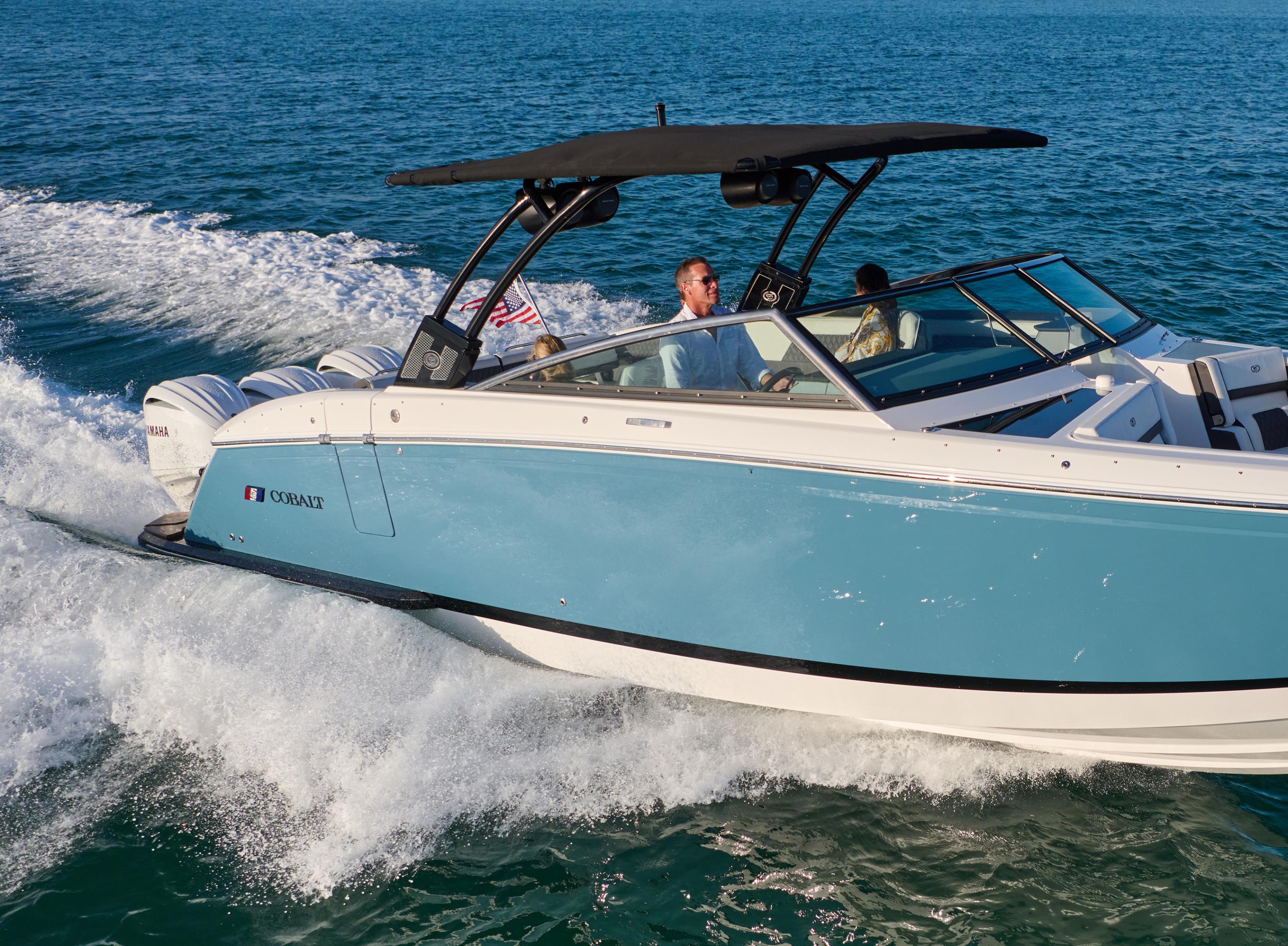 Couple aboard a blue Cobalt outboard-class boat running at speed with a wake tower across open ocean water
