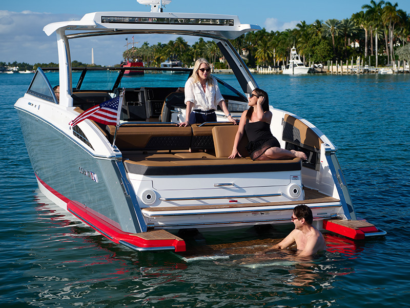 Cobalt R33 Sterndrive aft-facing rumble seat with couple relaxing on swim platform anchored in warm blue water