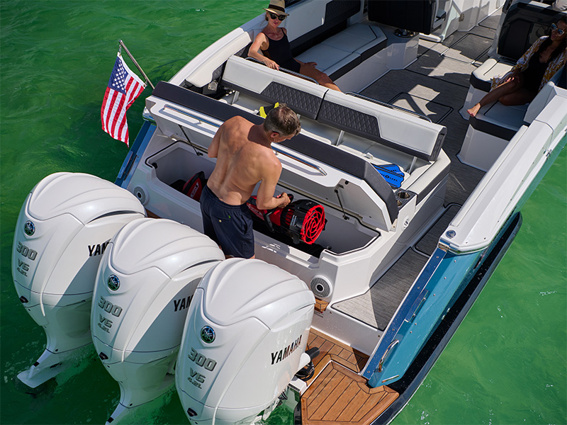 Cobalt R33 Coastal aft storage compartment open with gear stored beside triple Yamaha outboard engines on teal water