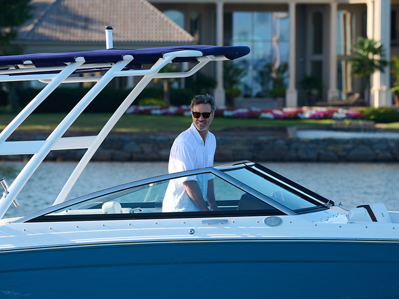 Man at the helm of a Cobalt R4 Coastal featuring stainless steel windshield trim and white tower against a sunset over calm lake water