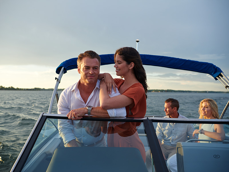 Couple leaning on stainless steel windshield trim of Cobalt R4 Sterndrive at sunset on open water
