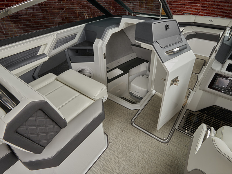Cobalt R6 Coastal head compartment open door revealing marine toilet beside gray upholstered interior seating