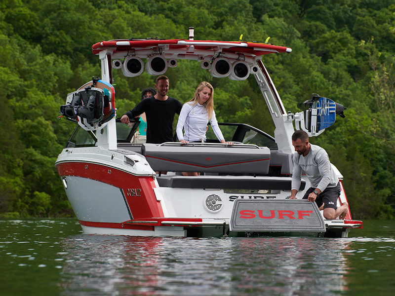 Cobalt R6 Surf electric swim step deployed with crew aboard and SURF branding on stern at forested lake