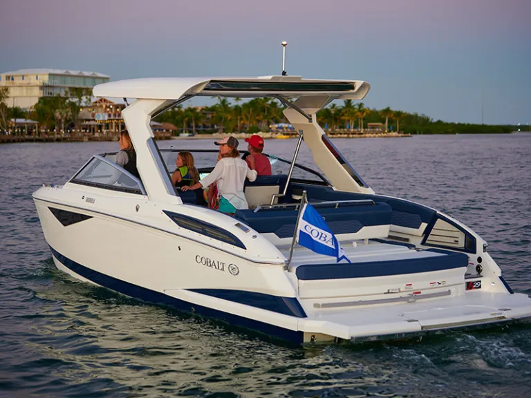 Cobalt A29 from the stern at dusk in tropical waters with hydraulic swim platform lowered, family aboard, and Cobalt flag flying